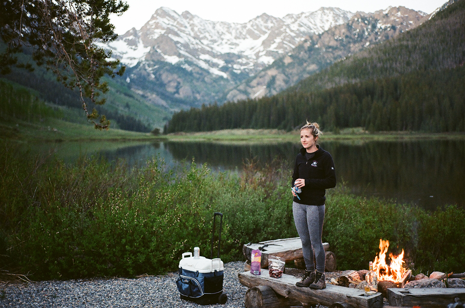 A woman stands at the campfire surrounded by camping gear