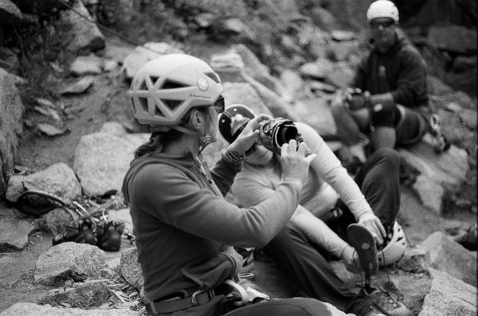 A woman shows her climbing shoes to her friends at the base of a rock climb