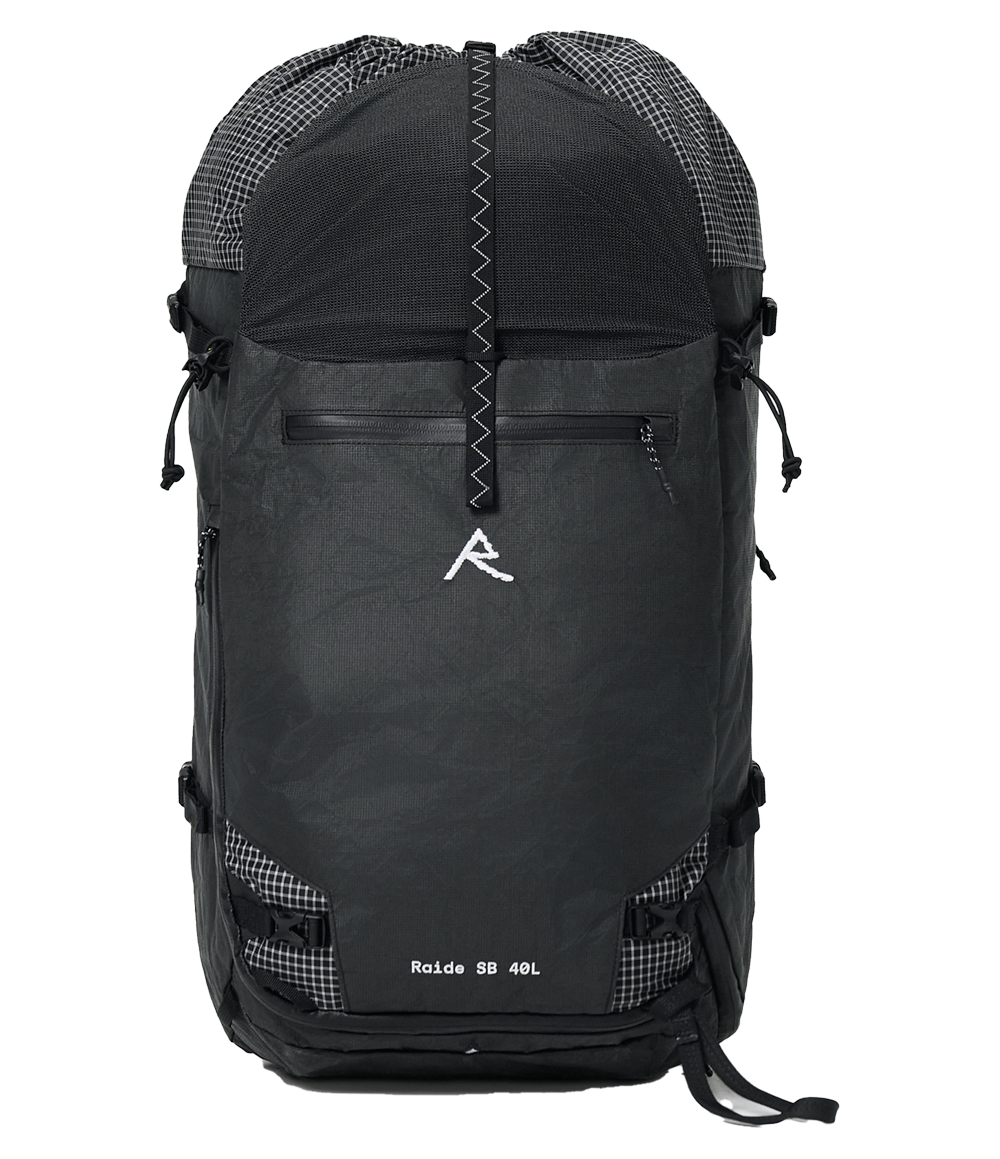 Raide SB 40L backcountry ski pack in Black with stowable roll top extended, showing front panel with white Raide logo, zippered pocket, compression straps, and gridded ripstop fabric accents on top and bottom corners