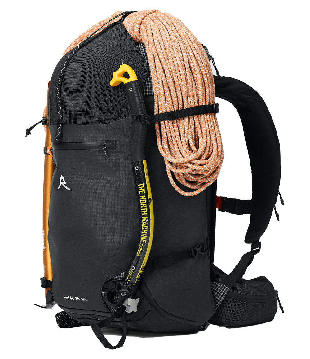 Raide SB 40L backcountry ski pack in Black with orange climbing rope lashed to front, yellow avalanche probe visible in dedicated side pocket, and aluminum ice tool secured in carry system